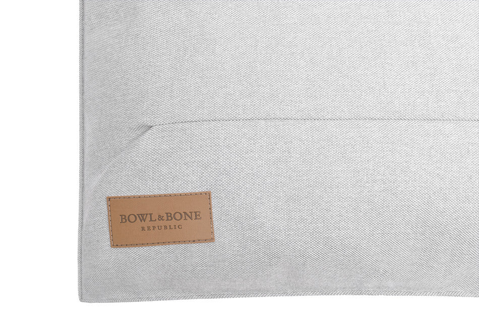 A Bowl&Bone Republic dog cushion bed URBAN grey pillow with a tan label on it.