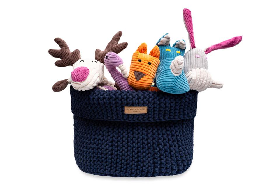 A knitted Bowlandbone basket for dog toys COTTON navy with stuffed animals in it.