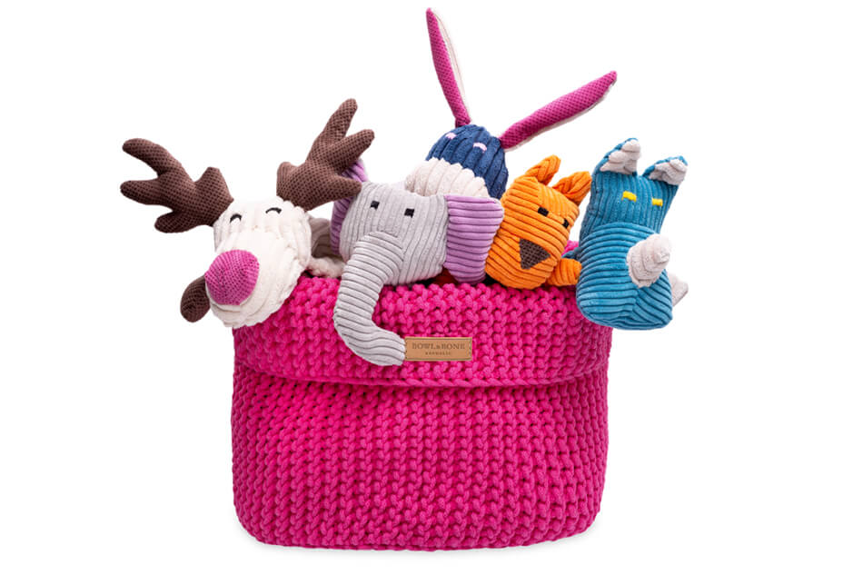 A Bowlandbone pink basket for dog toys COTTON with stuffed animals in it.
