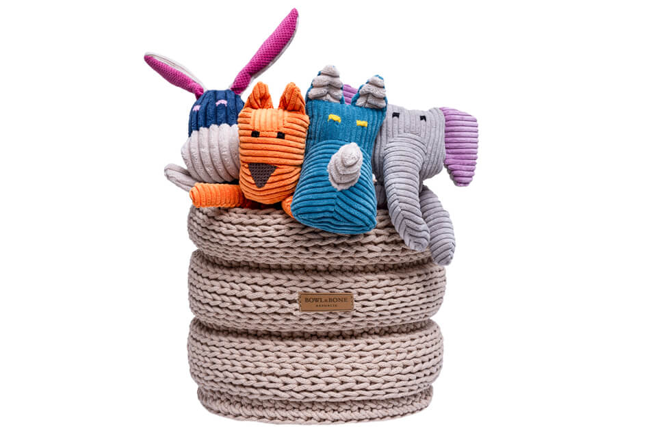 A group of stuffed animals in a Bowlandbone basket for dog toys RING beige.