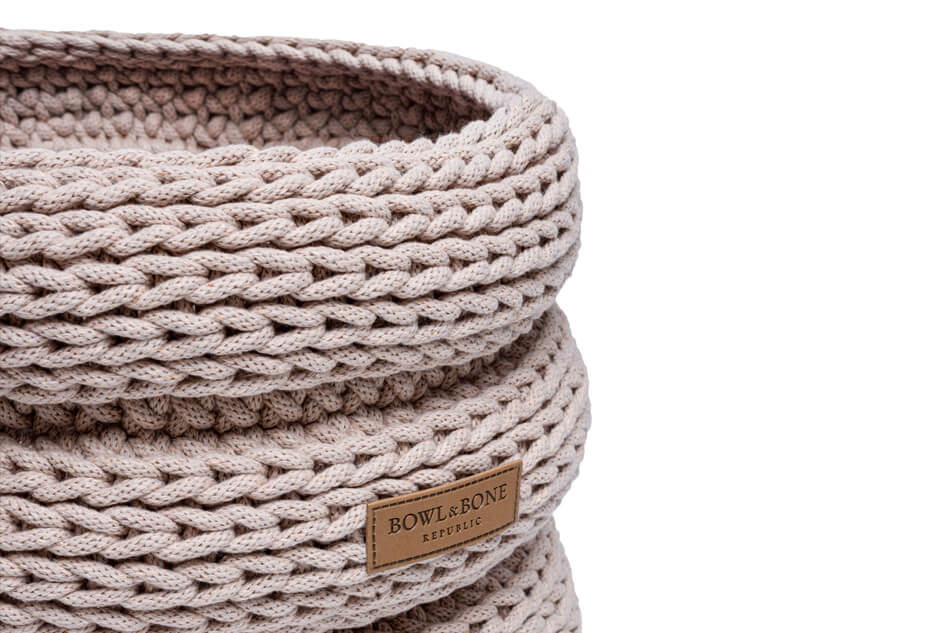 A knit Bowlandbone basket for dog toys RING beige with a brown label on it.
