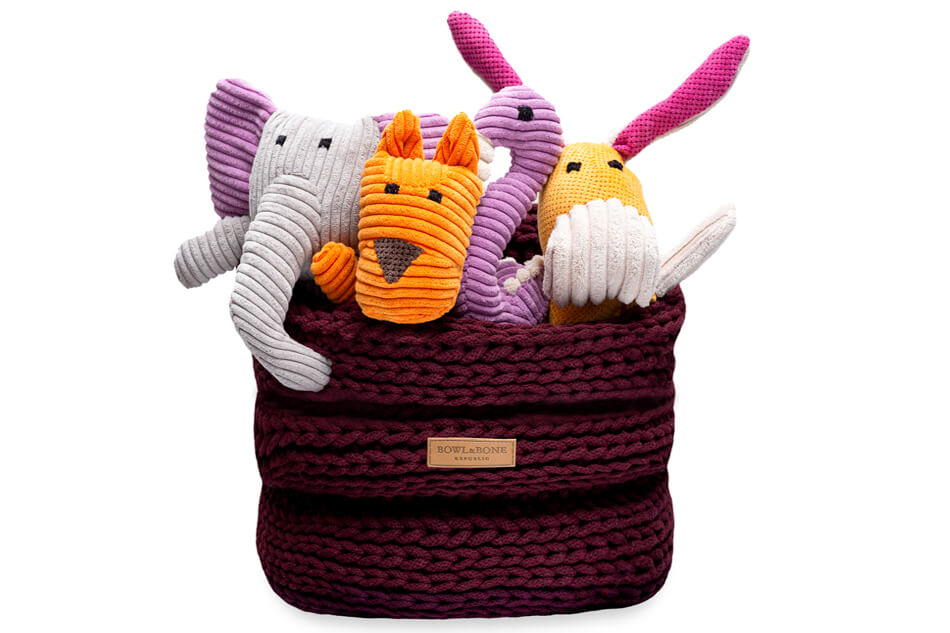 A group of stuffed animals in a Bowlandbone RING bordo basket for dog toys.