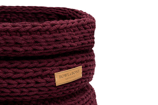 A Bowlandbone burgundy knitted basket with a wooden label.