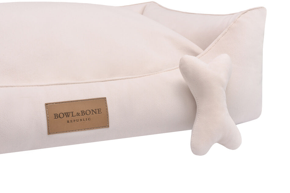 A cream colored dog bed from Bowl&Bone Republic with a bone decoration.