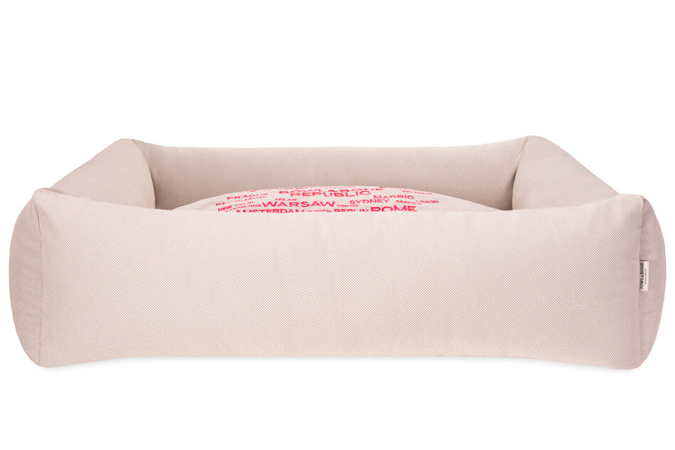 A Bowl&Bone Republic dog bed in COSMOPOLITAN cream with pink letters on it.