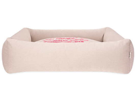 A Bowl&Bone Republic dog bed in COSMOPOLITAN cream with pink letters on it.