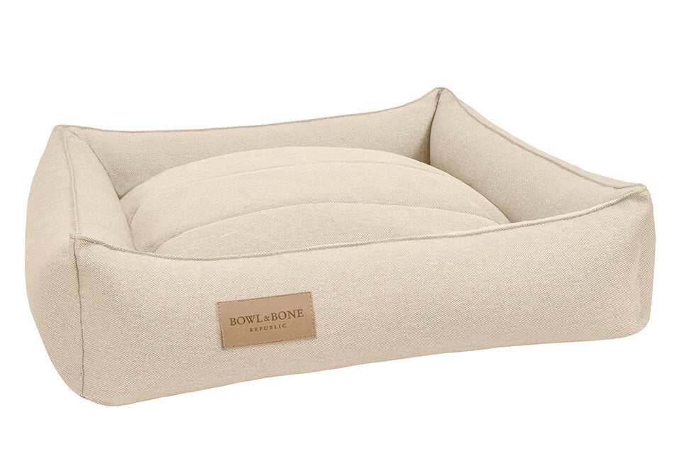 A Bowlandbone dog bed with an URBAN beige design featuring a tan label from Bowl&Bone Republic.
