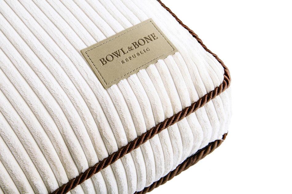 A white Bowl&Bone dog cushion bed DECO amber with a brown label on it.