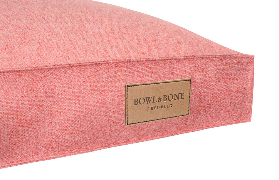 A pink Bowl&Bone dog cushion bed with a label on it.