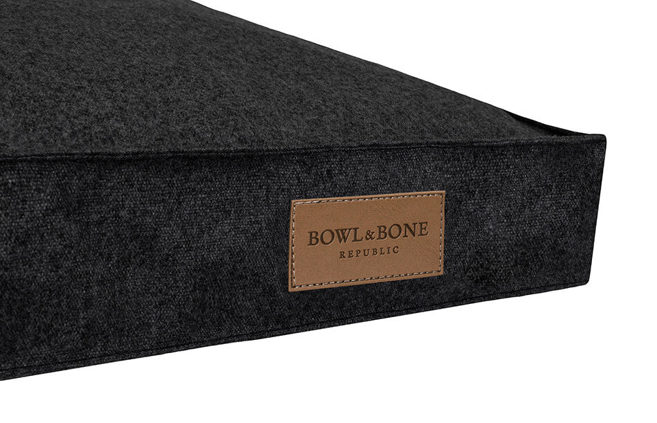 A black dog cushion bed from Bowl&Bone Republic with a leather label on it.