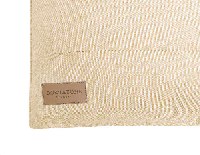 A dog cushion bed URBAN beige with a brown label on it by Bowlandbone, a Bowl&Bone Republic brand.