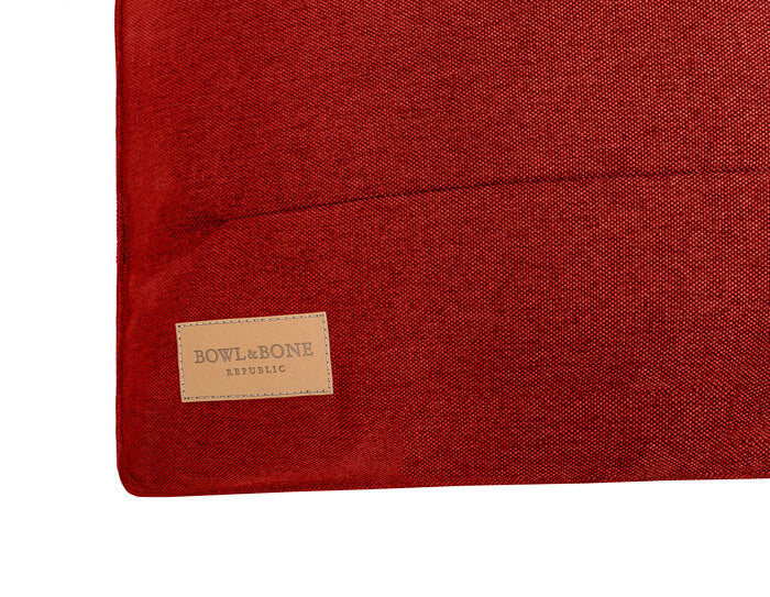 A dog cushion bed URBAN red with a tan label on it from Bowl&Bone Republic.