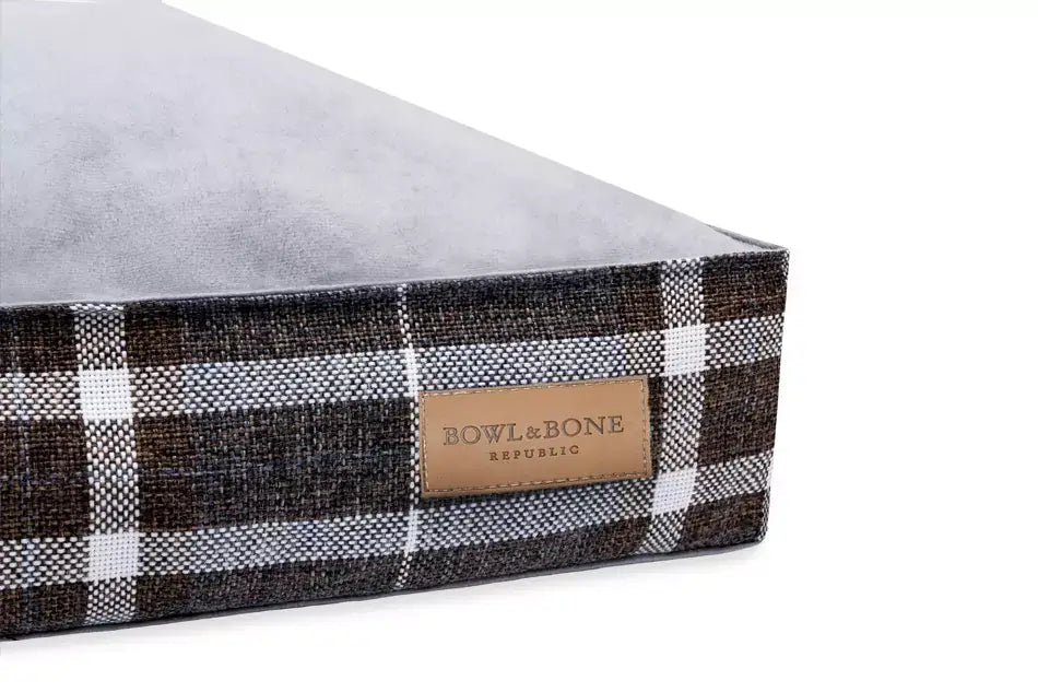 A brown and white plaid box with a label on it, containing the dog cushion bed SCOTT blue by Bowl&Bone Republic.