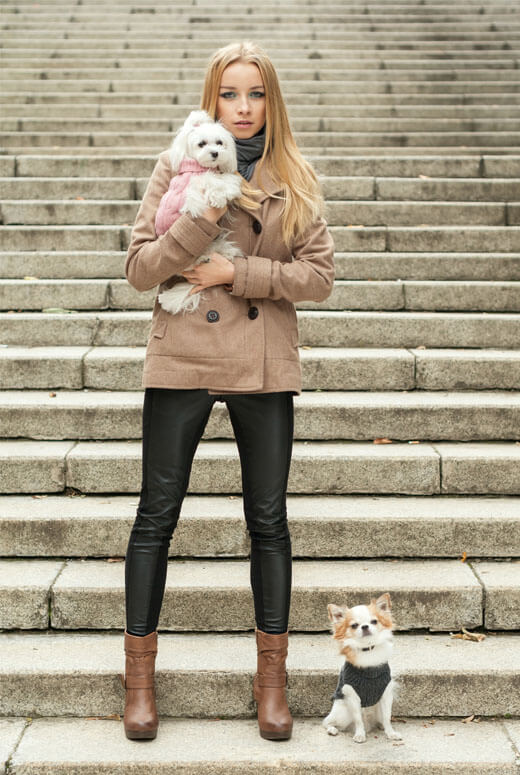 A woman wearing two Bowlandbone dog sweaters from Bowl&Bone Republic stands on the steps.