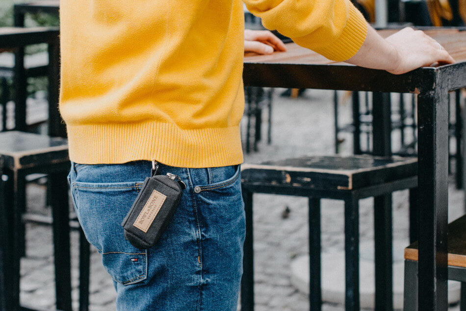 A man wearing a yellow sweater standing next to a table holding a Bowl&Bone Republic dog waste bag holder MINI navy.