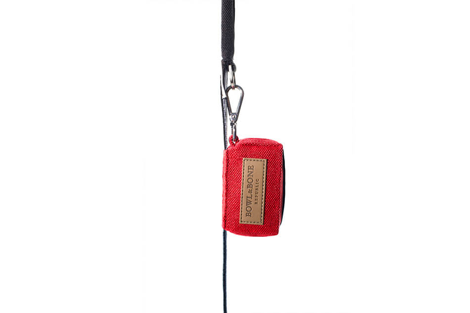 A red mini dog waste bag holder with a black handle attached to it from Bowl&Bone Republic.